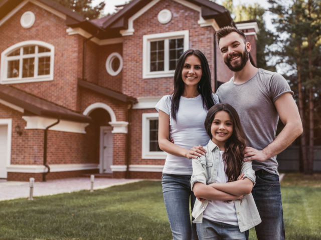 Happy,Family,Is,Standing,Near,Their,Modern,House,,Smiling,And